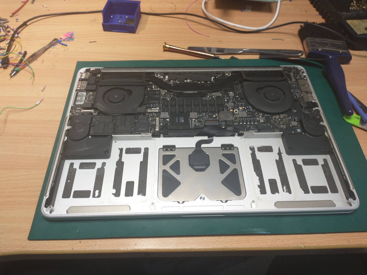 A laptop opened up on the repair bench — internals and logic board exposed, mid-service